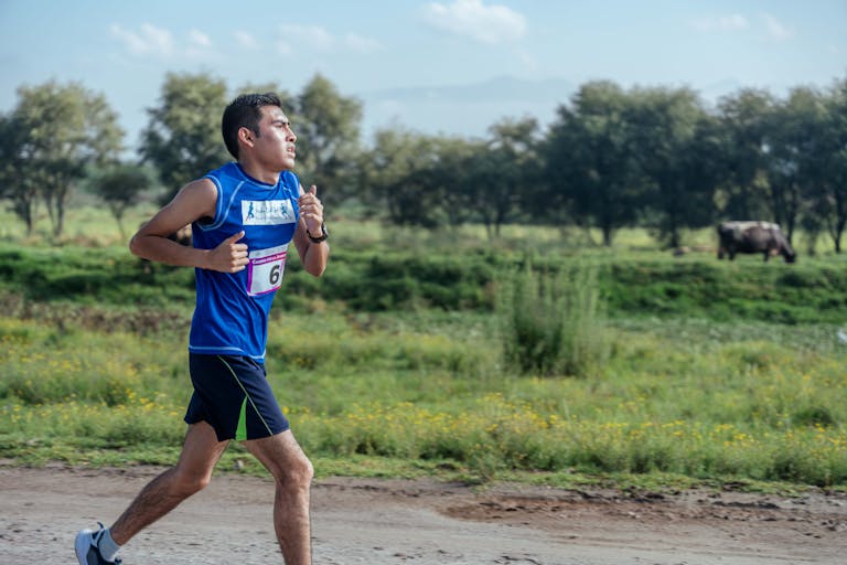 Mężczyzna uprawiający jogging na wiejskiej drodze w otoczeniu przyrody, ubrany w odzież sportową.