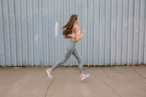 Wysportowana kobieta biegająca na świeżym powietrzu w sportowym staniku i legginsach. Ruch uchwycony w ciągu dnia.
