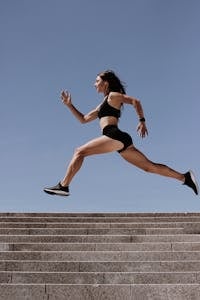 Energiczna kobieta w aktywnym stroju skacząca po schodach na zewnątrz, pokazująca sprawność i determinację.