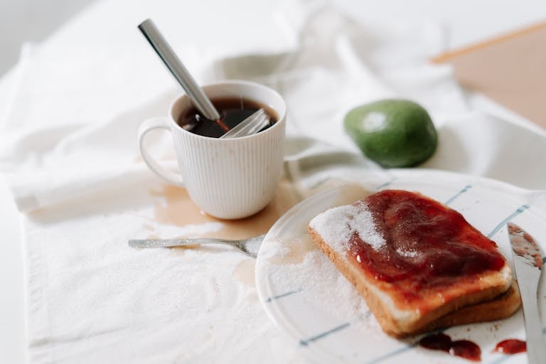 Przytulna, niechlujna scena śniadaniowa z kawą, rozsypanym cukrem i tostami z dżemem.