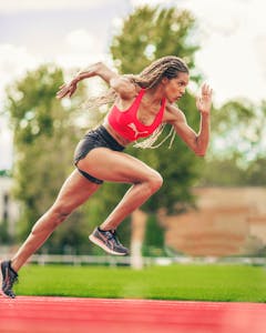 Zawodniczka w stroju sportowym biegnąca sprintem na bieżni, pokazująca siłę i szybkość. Ujęcie akcji na świeżym powietrzu.
