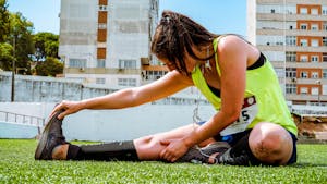 Młoda kobieta w neonowej kamizelce rozciągająca się na trawie, przygotowująca się do treningu na świeżym powietrzu lub biegu.