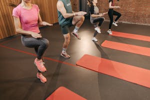 Grupa wykonuje ćwiczenie „wysokie kolana” w sali fitness wyposażonej w maty do jogi.