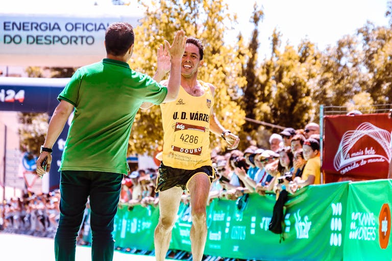 Mężczyzna biegacz przybija piątkę kibicowi na mecie biegu w jasnym świetle dziennym.