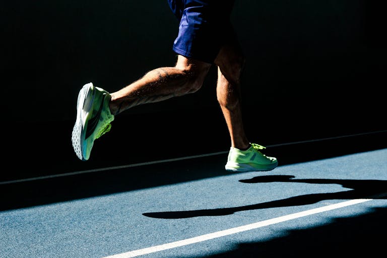 Nogi biegacza w ruchu rzucają cień na bieżnię.