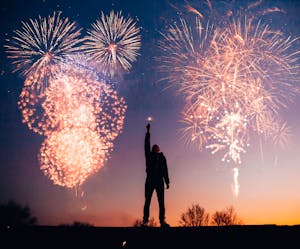 Osoba świętuje pod rozświetlonym niebem wieczornym fajerwerkami.