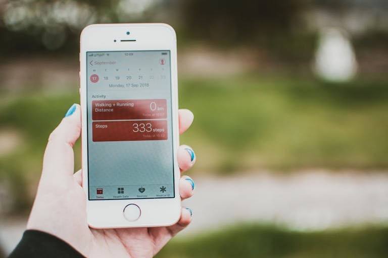 Osoba trzyma smartfon z aplikacją fitness, która pokazuje liczbę kroków i odległość pokonaną na świeżym powietrzu.