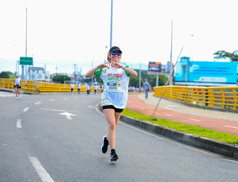 Wesoła biegaczka wykonująca gest serca podczas biegu ulicznego.