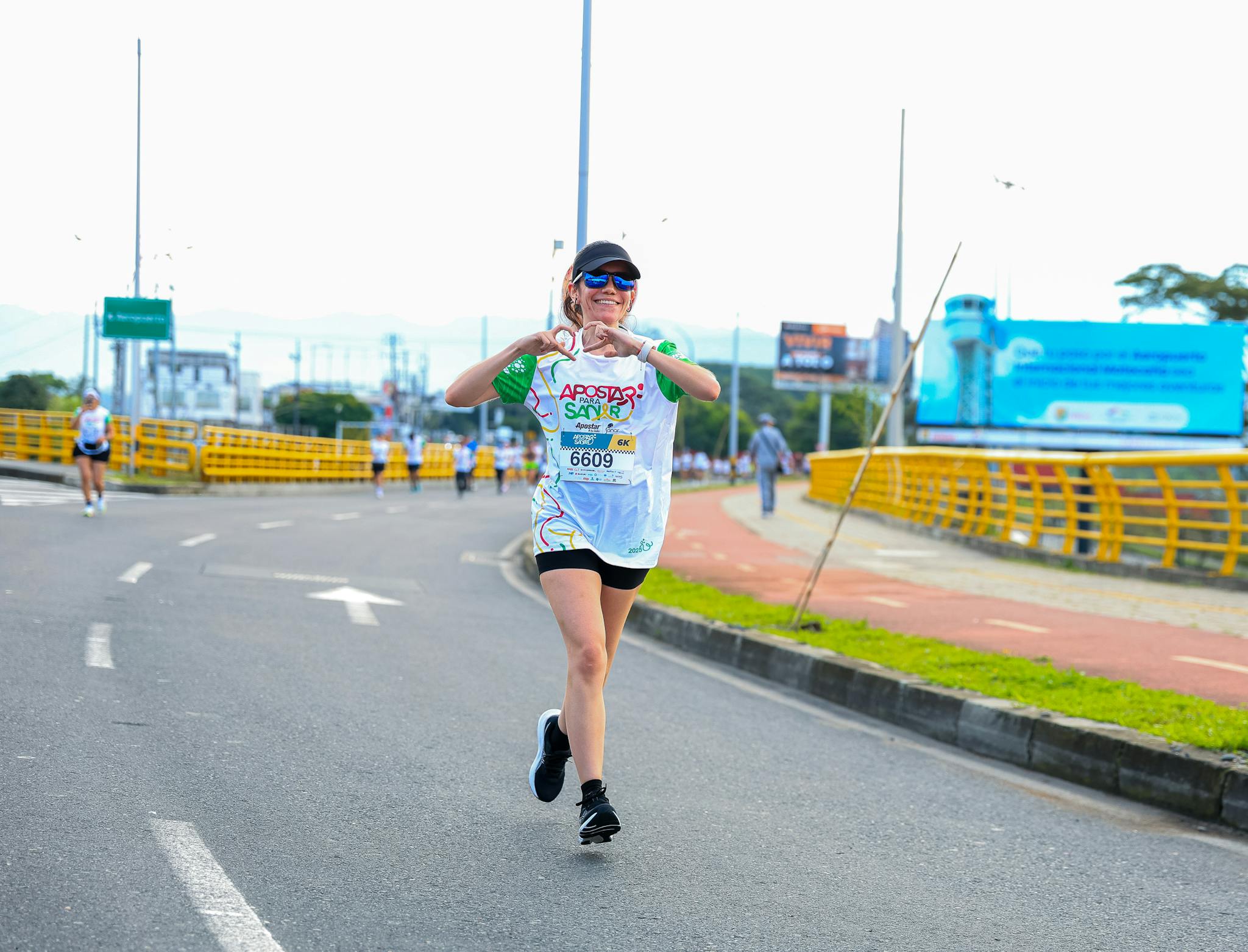 Wesoła biegaczka wykonująca gest serca podczas biegu ulicznego.