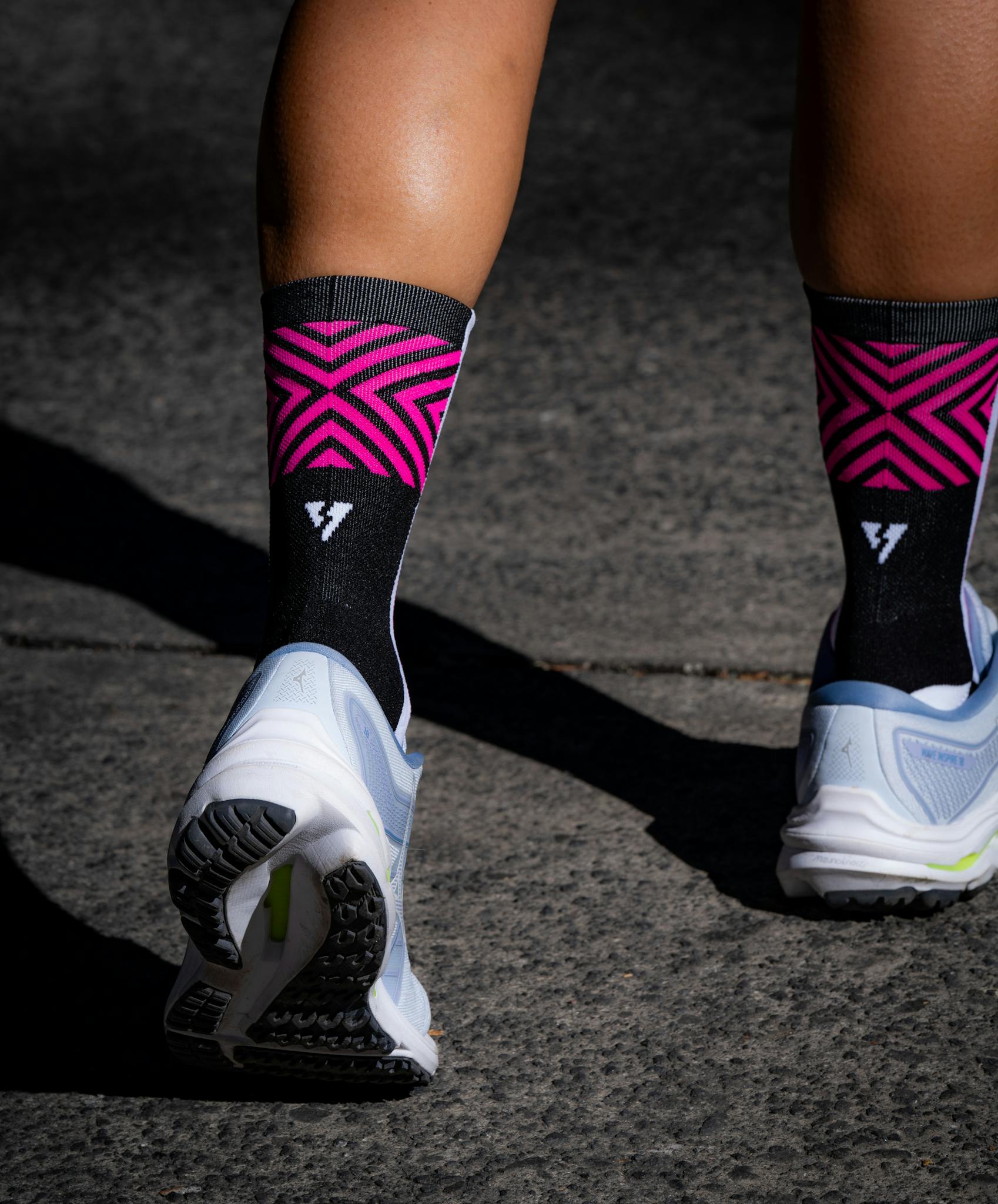 Zbliżenie na nogi sportowca w różowych skarpetkach i tenisówkach na chodniku na świeżym powietrzu.
