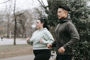 Widok z boku kobiety z nadwagą w stroju sportowym biegającej z trenerem w miejskim parku w ciągu dnia.